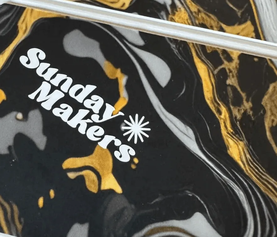 The Sunday Makers logo printed in white on a marbled black and gold card