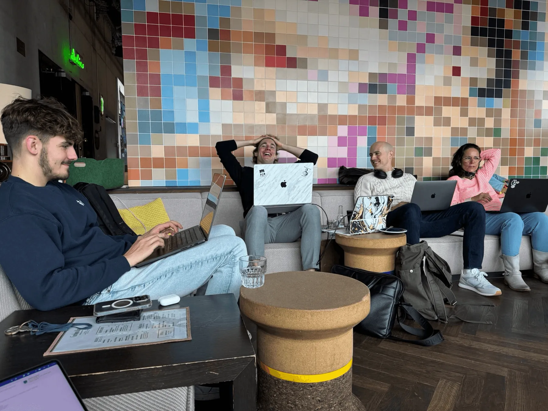 Makers on a long sofa with laptops in front of a pixel mosaic wall