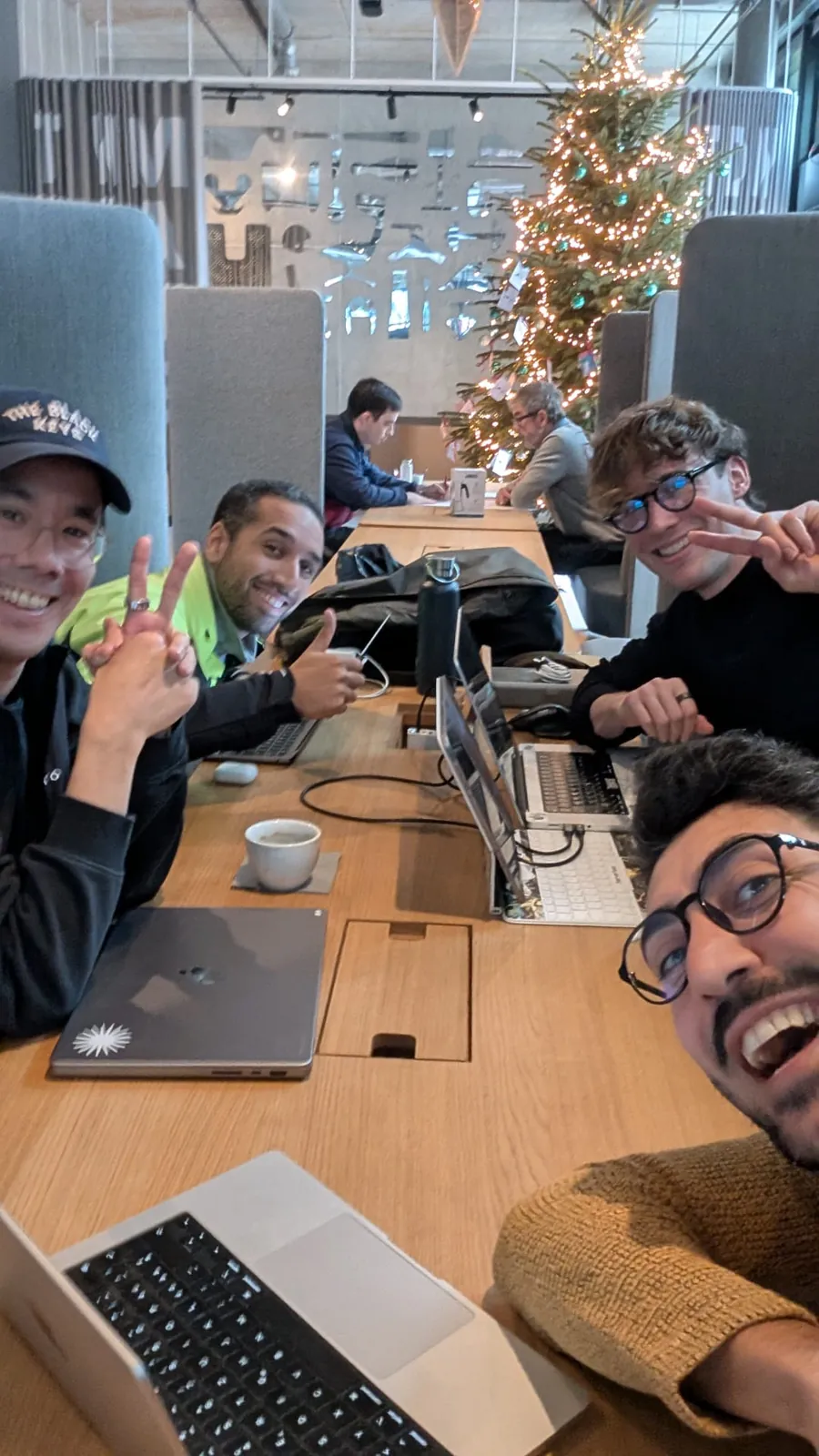 A group of makers taking a selfie at a long table, a Christmas tree behind them